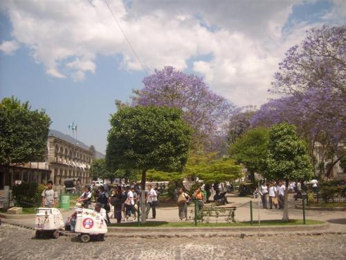 School kids, Mayan women in traditional dress, street vendors, and others in the sunny Parque Central, Antigua, Guatemala.