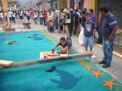 Man working on an ocean themed alfombra using a stencil and colored saw dust in town of Jocotenango, near Antigua, Guatemala.